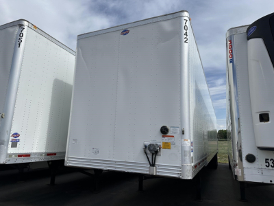 Front view of a white Utility 4000D-X trailer showing its nose with hitch and side numbers 7042. Other trailers flank on either side.