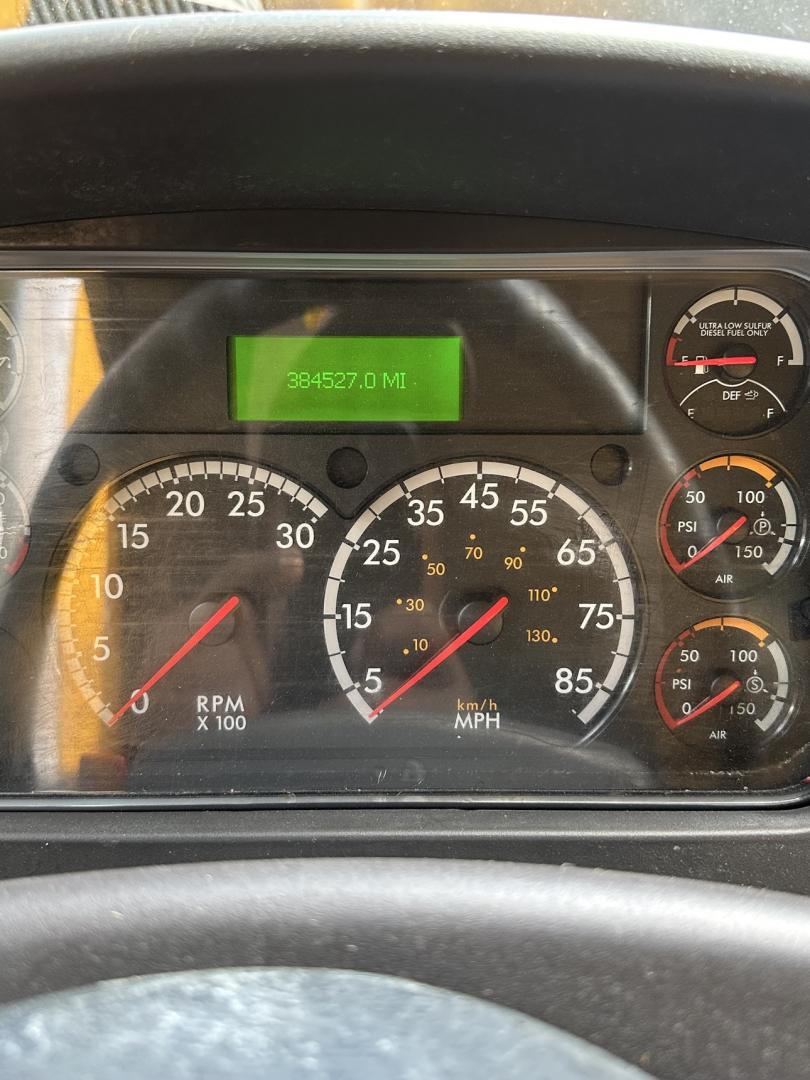 Dashboard of a Freightliner M2 106 showing gauges and a green digital odometer reading 384527.0 MI.
