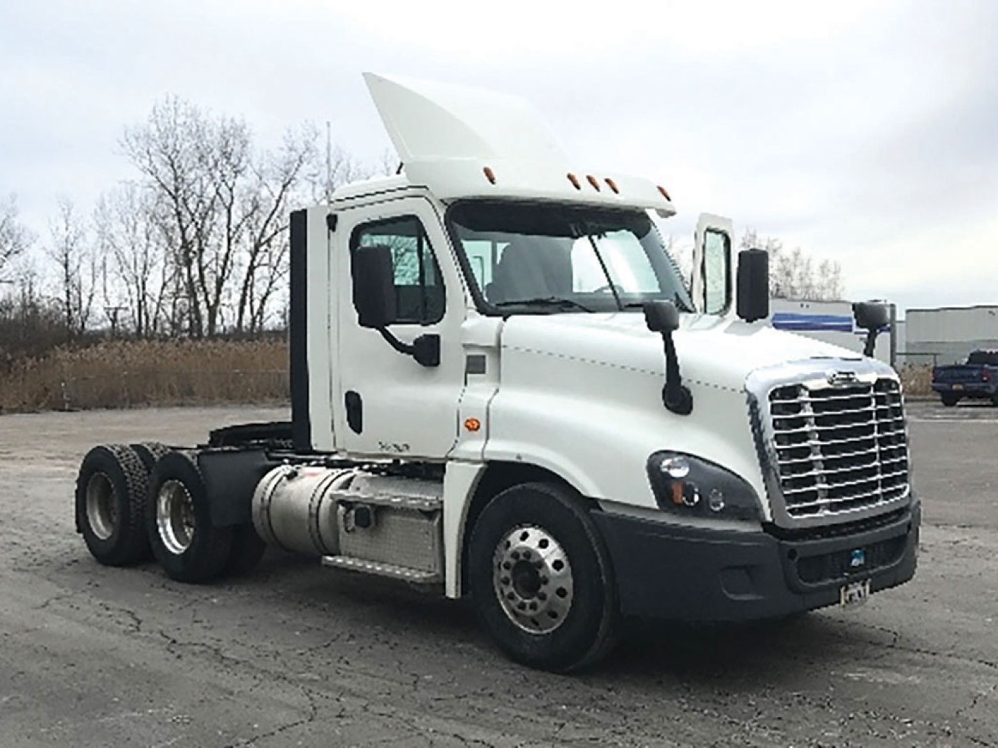 Truck cab side view showing Freightliner Cascadia 113 day cab with white paint and exposed fuel tanks.