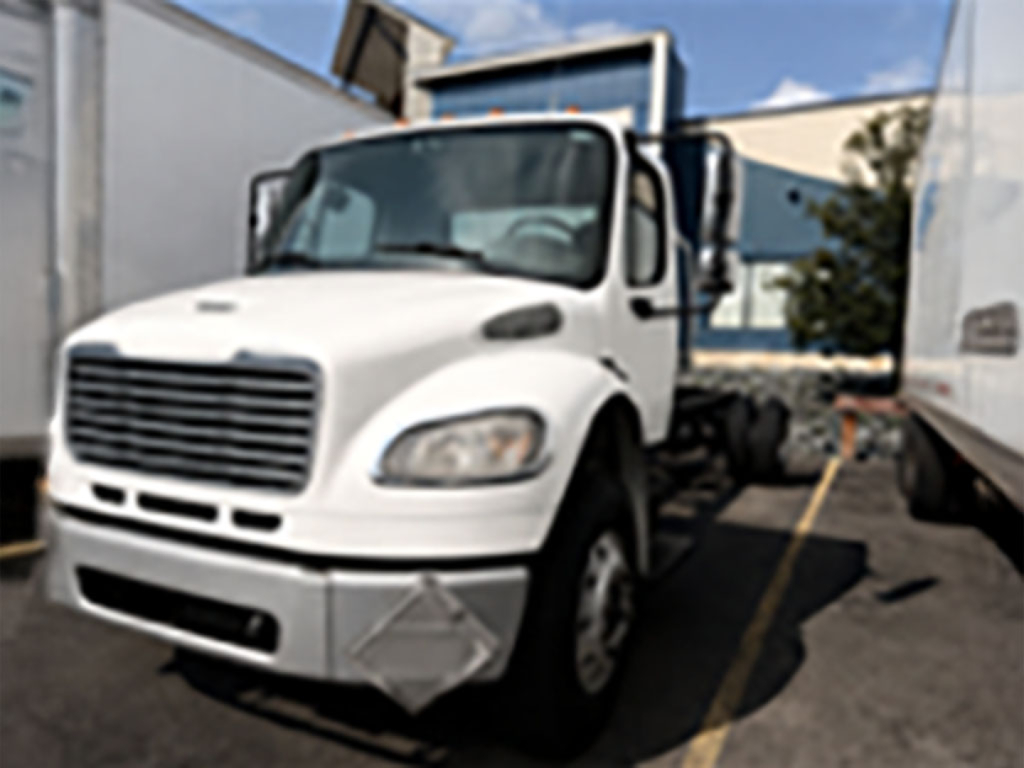 White Freightliner M2 106 cab and chassis truck showing front grille and bumper with side mirror; no visible text readable on vehicle.