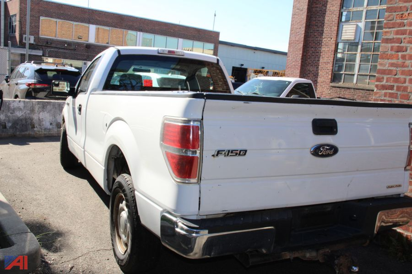 Ford F-150 pickup tailgate with F-150 badge and Ford oval logo in back, white 2014 model, truck in an outdoor lot.