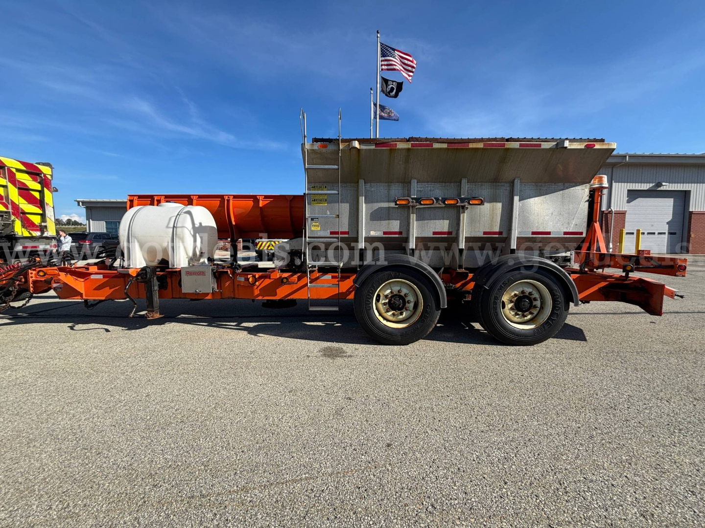 Side view of 2013 Mack GU Granite plow truck chassis with large dump bed, dual rear axles, and hose/tank components visible.