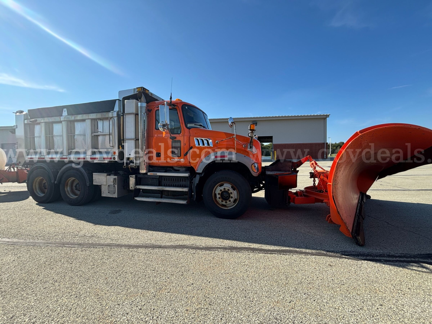 Mack GU Granite dump truck with snow plow blade attached, side view showing orange cab and black dump bed.