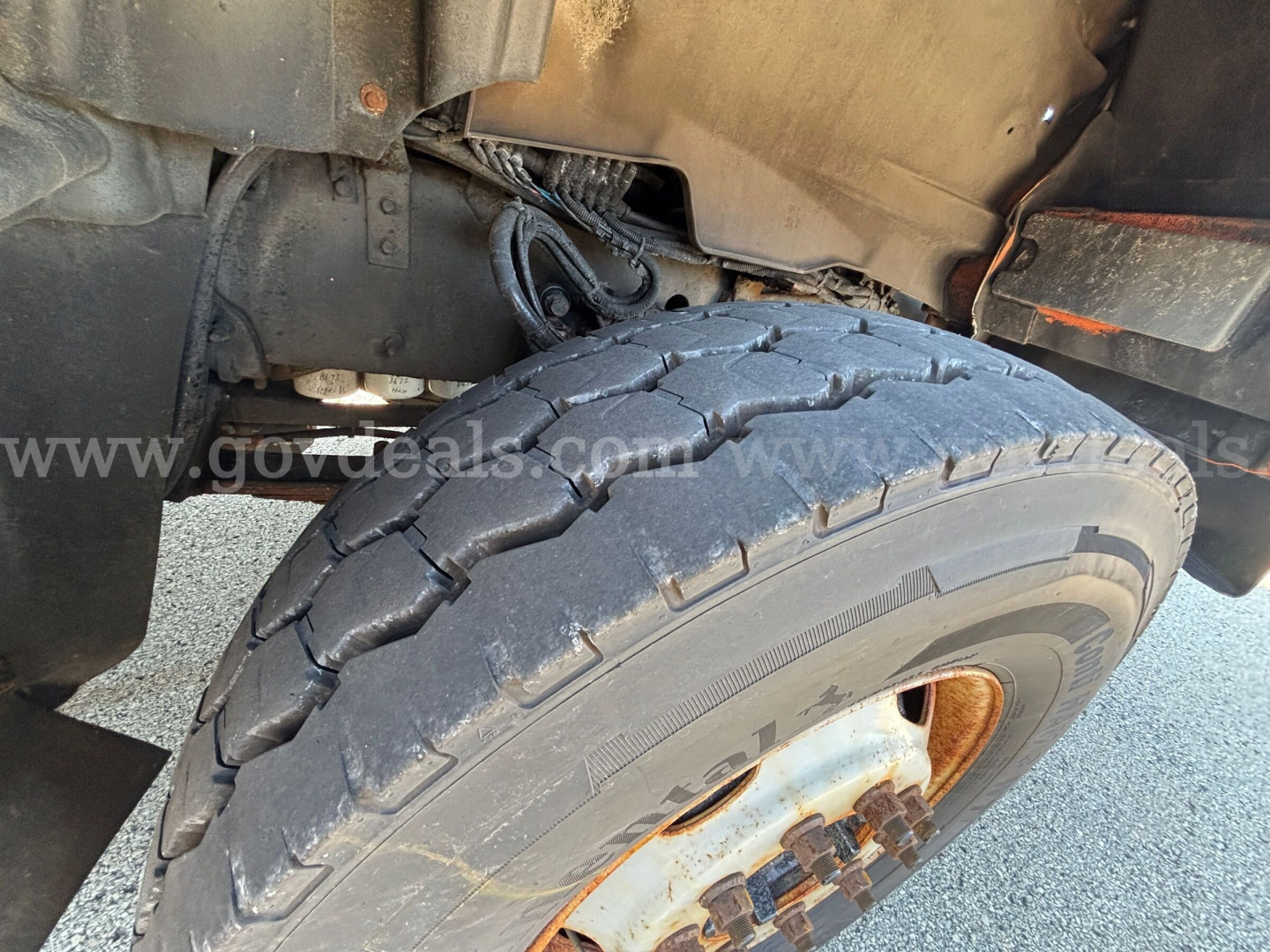 Truck front-left wheel well showing heavy-duty tire and wheel assembly on a Mack GU Granite cab. Visible suspension components and body panels.