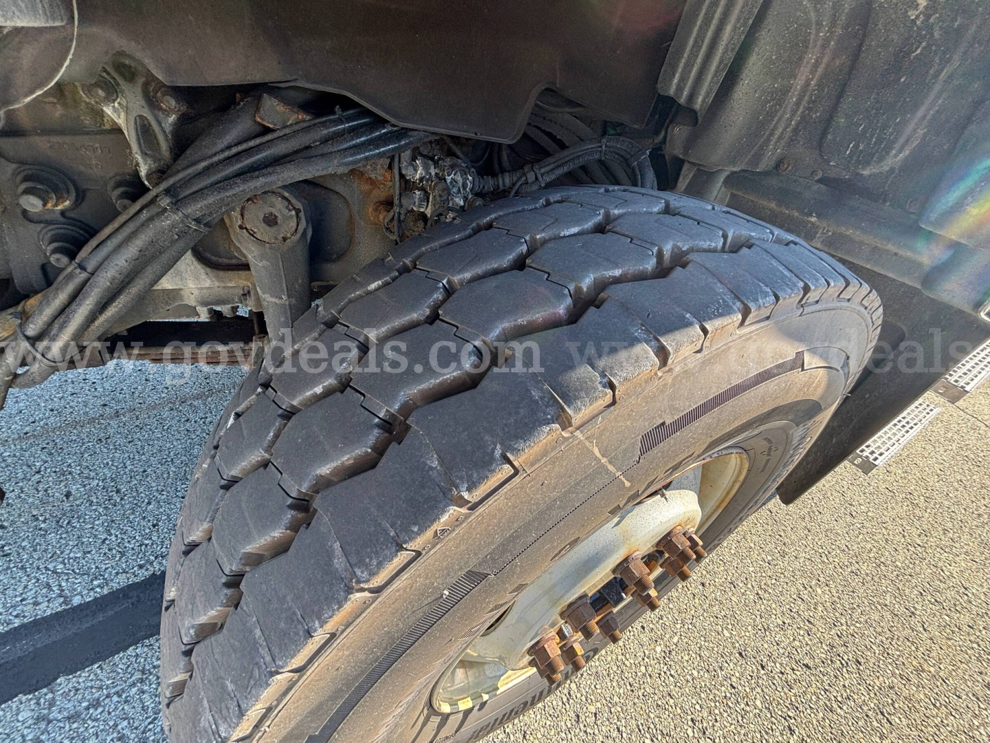 Front wheel and tire of a 2013 Mack GU Granite truck showing heavy-duty dual rear axle and wheel, with visible suspension components and tire tread.