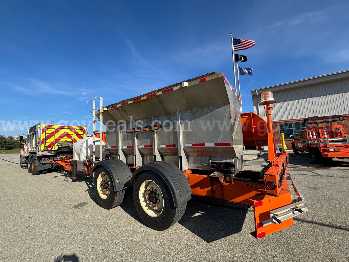 Truck bed showing dump trailer with orange frame and three axles, wheel tires, raised bed, and reflective safety stripes.