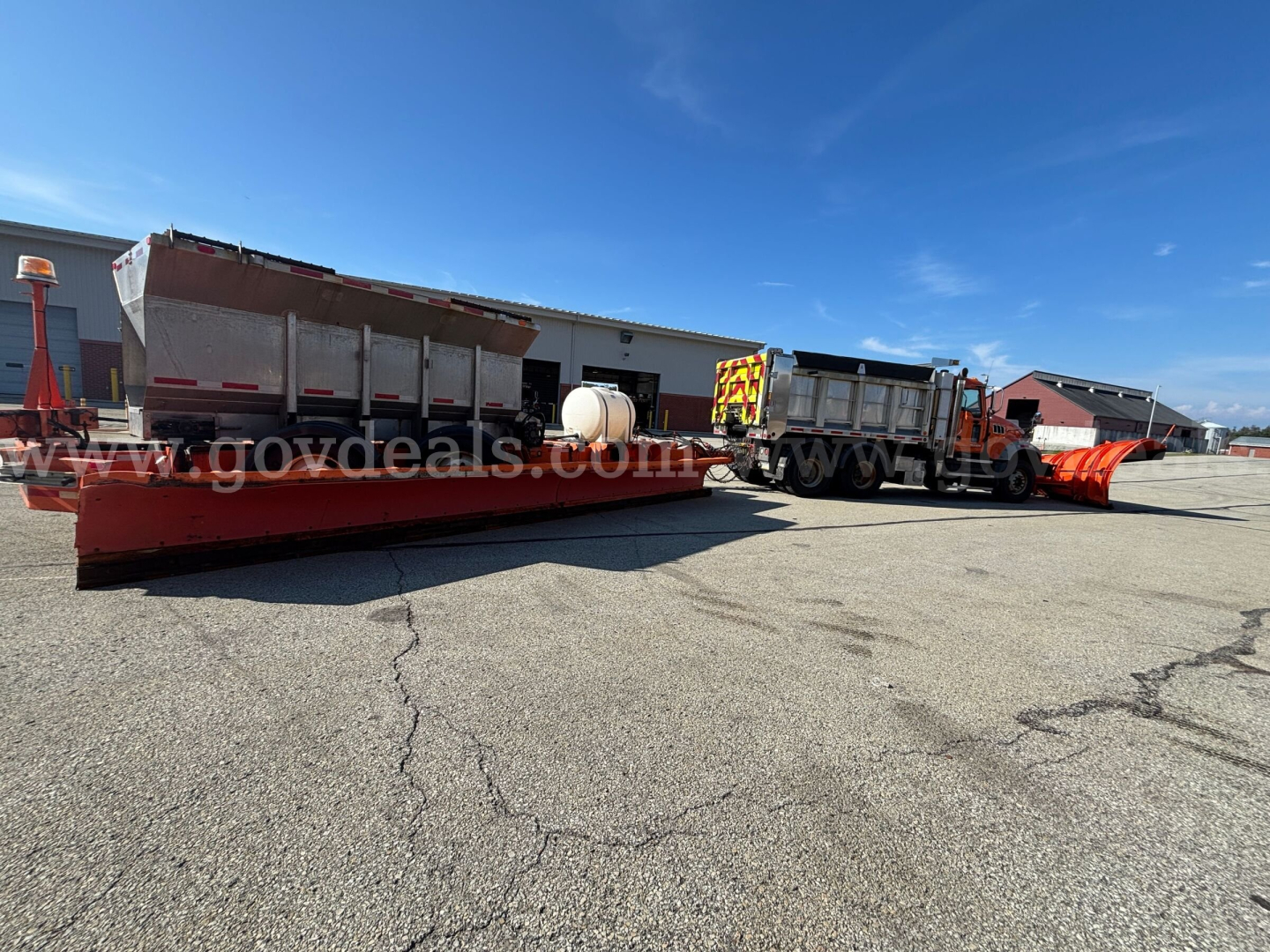 Truck-mounted plow and granular material body on Mack GU713 Granite chassis, side view, with orange snow plow blade and flatbed hopper in an industrial lot.