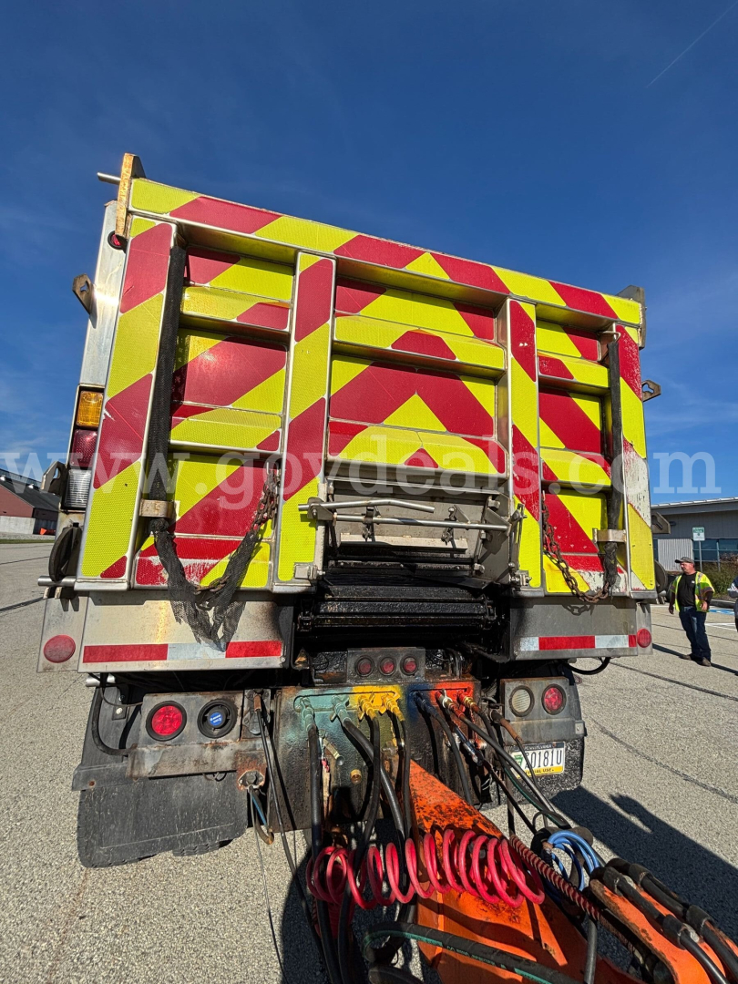 Rear view of a 2013 Mack GU (Granite) GU713 plow truck showing high-visibility chevron pickup in yellow and red, tow hoses, and rear lights.