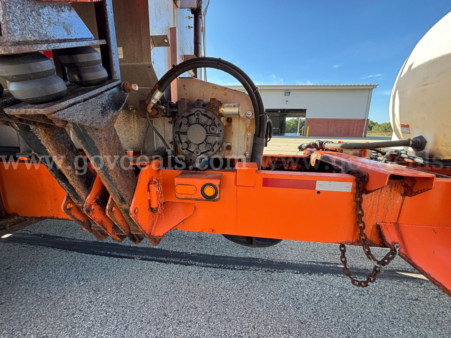 Orange undercarriage of a Mack GU (Granite) GU713 plow truck showing hydraulic hoses, mechanical joint, and a chain attached to the chassis.