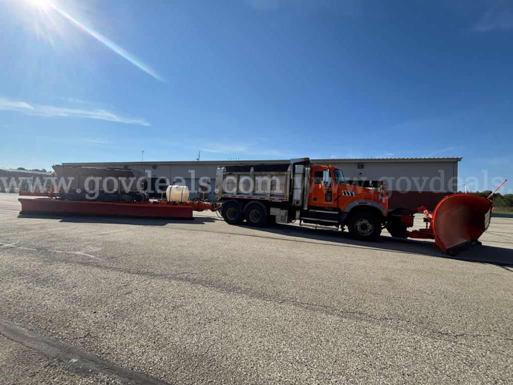 Truck with large plow assembly and flatbed trailer, orange cab, Mack Granite GU713 pulling a long plow attachment.