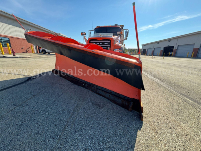 Front view of a Mack Granite GU713 snow plow truck with an orange and black plow blade raised, truck cab visible in background.