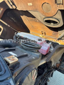Mack GU Granite truck engine bay view showing coolant reservoir, power steering fluid? container, and assorted hoses near the firewall.