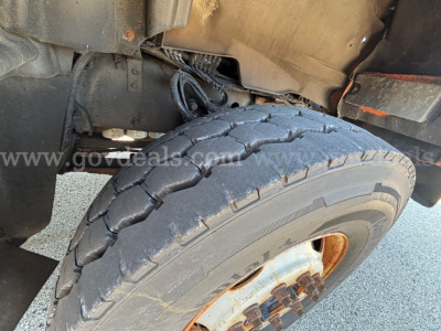Truck front-left wheel well showing heavy-duty tire and wheel assembly on a Mack GU Granite cab. Visible suspension components and body panels.