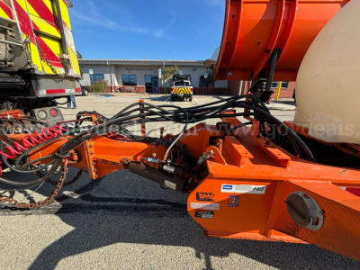 Front left view of a 2013 Mack GU Granite plow truck chassis with orange equipment and hydraulic hoses; VIN tag and stock number not visible; foreground showing hydraulic winch area and control components.