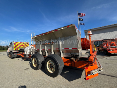 Truck bed showing dump trailer with orange frame and three axles, wheel tires, raised bed, and reflective safety stripes.