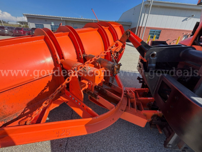 Snow plow blade and housing components on a Mack Granite GU713 truck, orange color with chains and linkage visible, plow assembly in o view