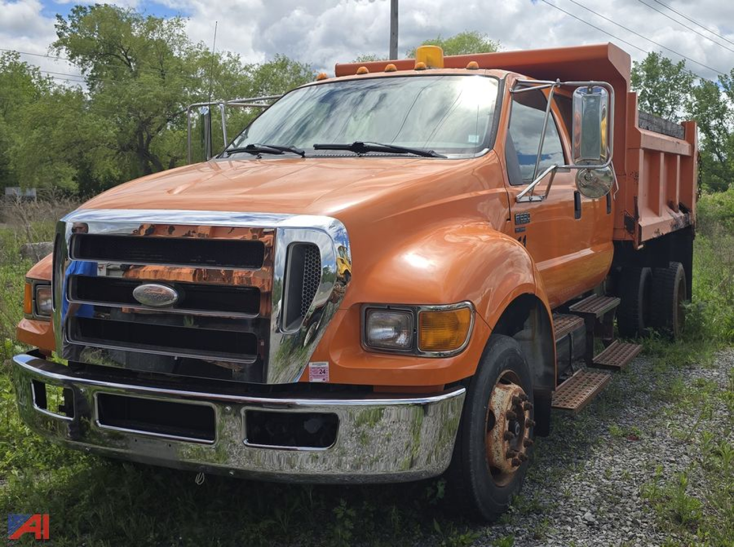 Dump truck with orange cab and bed, front chrome grille, Ford emblem, dual headlights, side mirrors, and steps. Visuals show a heavy-duty dump truck with large front bumper; no legible small text visible.