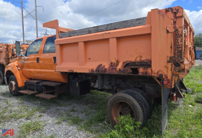 Ford F650 dump truck in-service with orange cab and dump bed, side view showing dual rear wheels, hydraulic bed, and loader steps