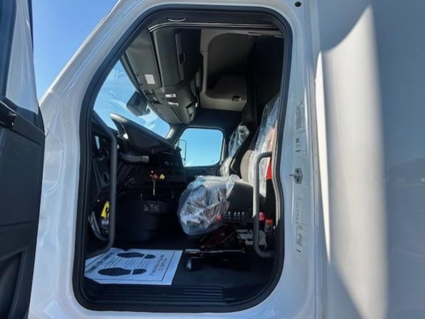 Truck cab interior of a 2023 Freightliner Cascadia 126 featuring a steering wheel, dashboard, and driver seat area visible through open door.
