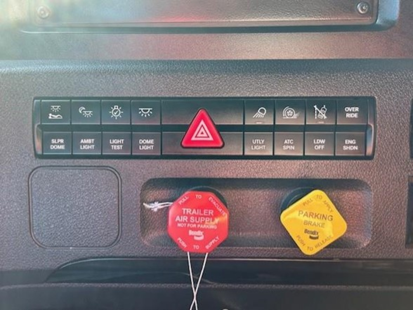 Dashboard control panel of a Freightliner Cascadia 126 showing various switches and two colored caps labeled trailer air supply and parking brake.