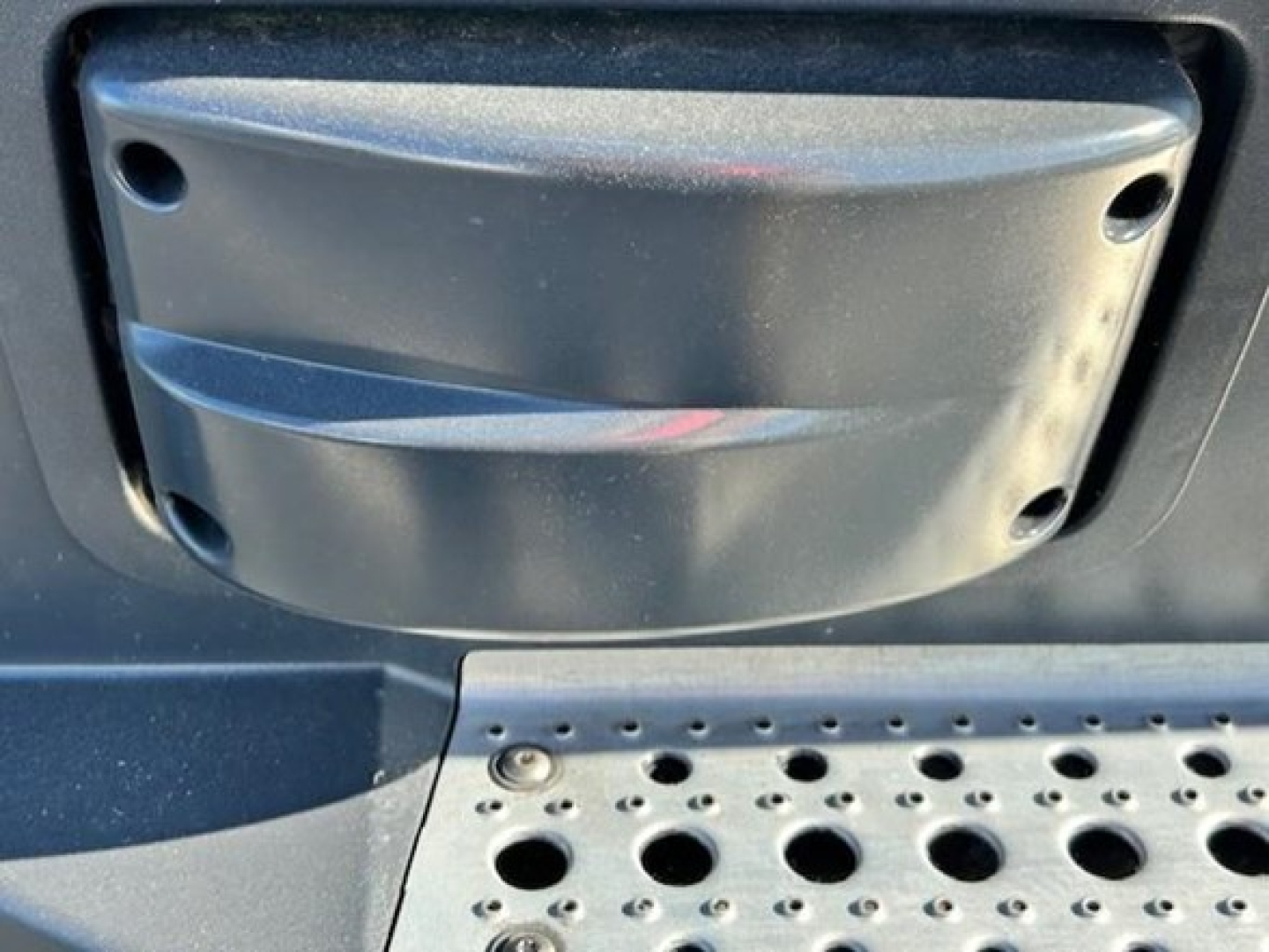 Conventional sleeper truck exterior step and rear sill with textured metal surface and circular drain holes.