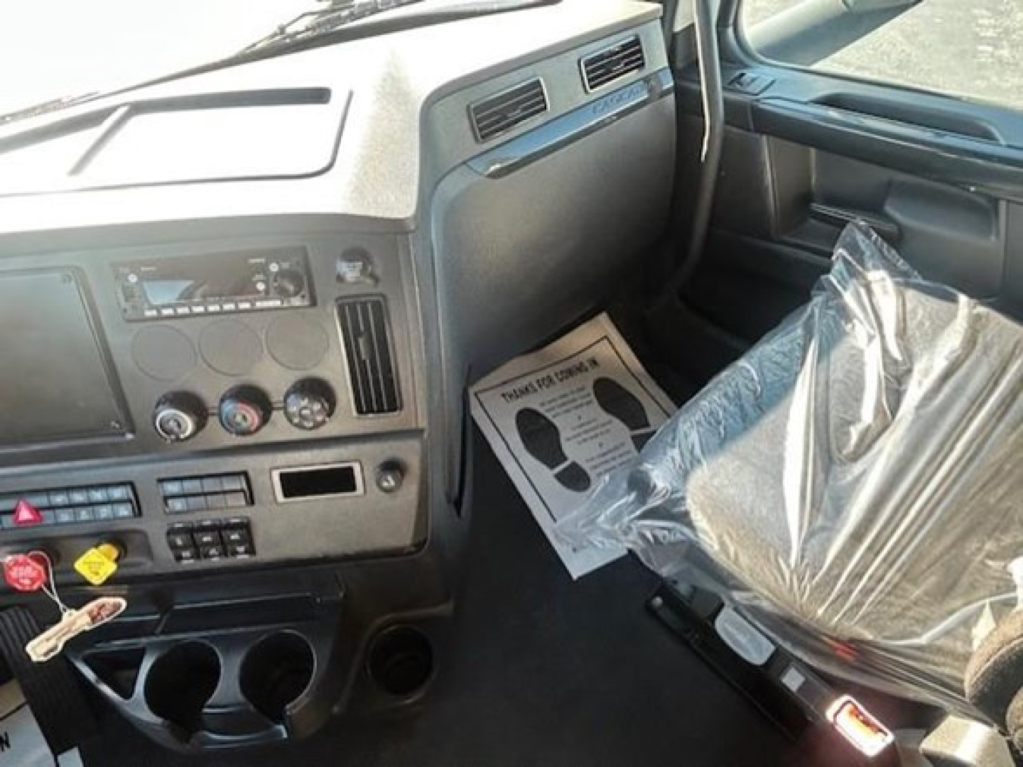 Interior of a 2023 Freightliner Cascadia 126 truck cab showing dashboard controls and driver seat wrapped in plastic.