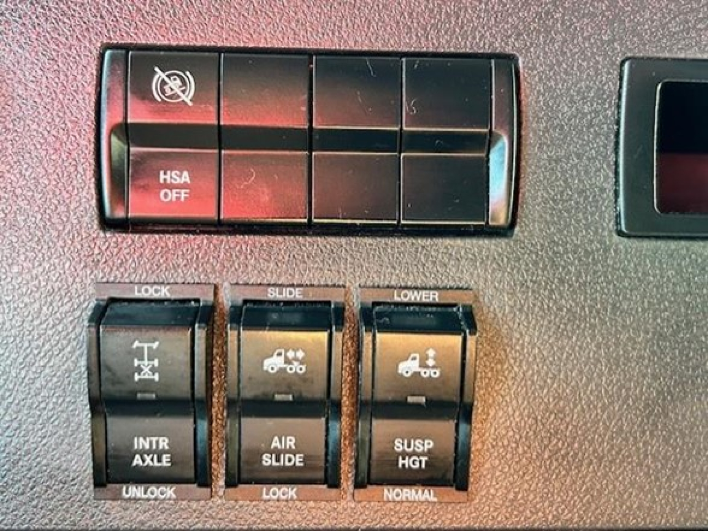 Cab interior switches and controls in a Freightliner Cascadia showing HSA OFF, LOCK/SLIDE/LOWER toggles for INTR AXLE, AIR SLIDE, SUSP HGT.
