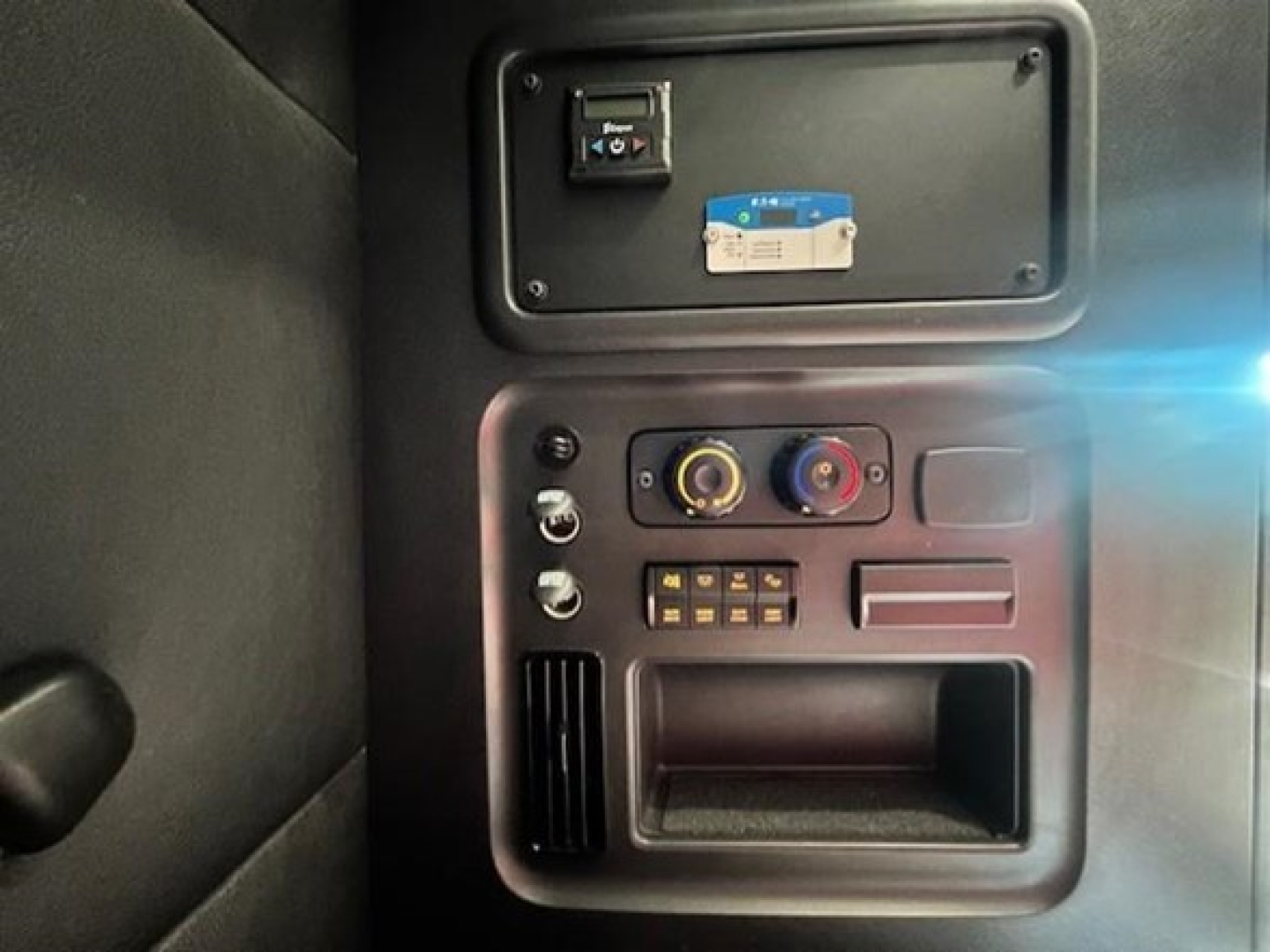 Dashboard panel showing power/auxiliary controls in Freightliner Cascadia cab with switches, knobs, and a small storage pocket.