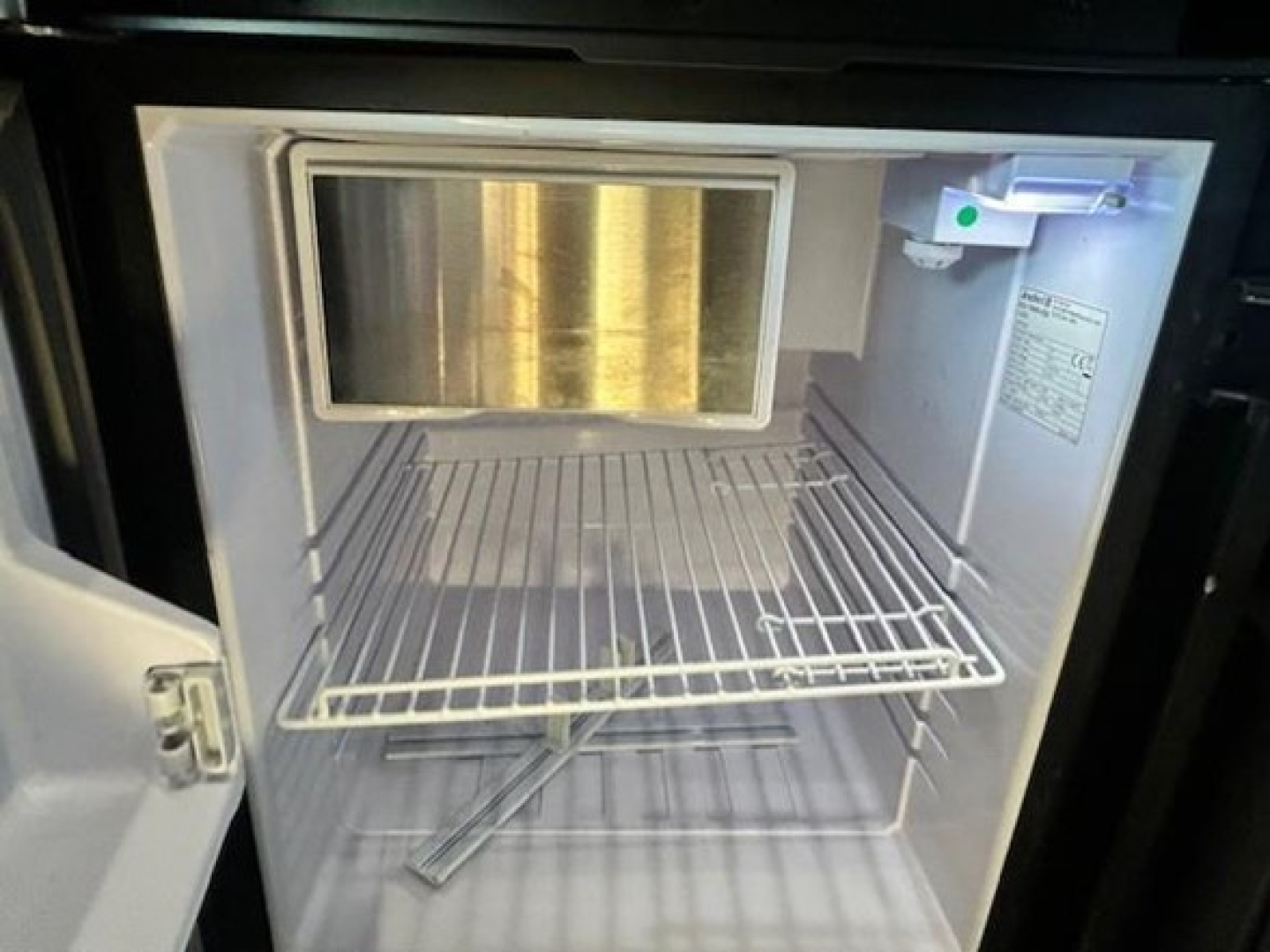 Freezer compartment with empty wire shelf and small light, part of a Freightliner Cascadia truck interior.
