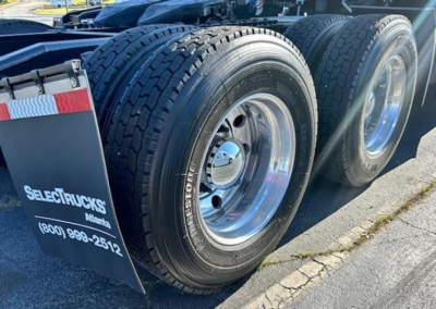 Front dual rear axle wheels of a Freightliner Cascadia sleeper truck with chrome rims and mud flaps displaying Select Trucks Alaska contact information.