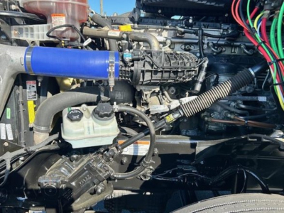 Parts of Freightliner Cascadia 126 engine bay showing blue intercooler hose, air intake, coolant reservoir, and wiring harnesses.
