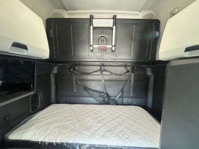 Freightliner Cascadia truck cab sleeper interior showing bunk area with mattress and storage compartments.