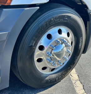 Truck wheel and tire close-up showing Goodyear/coach tire and polished hubcap with lug nuts on Freightliner Cascadia 126.