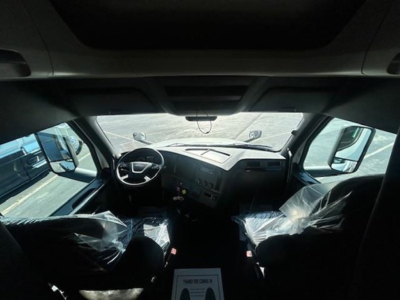 Freightliner Cascadia cab interior view from front with steering wheel and dashboard; plastic-covered seats visible.