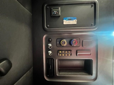 Dashboard panel showing power/auxiliary controls in Freightliner Cascadia cab with switches, knobs, and a small storage pocket.
