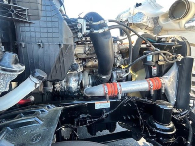 Truck engine bay of a Freightliner Cascadia showing exposed engine components, hoses, and metal piping.