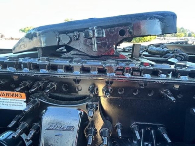 Truck cab with top air deflector and numerous hydraulic lines in engine bay; metallic components and a label visible.
