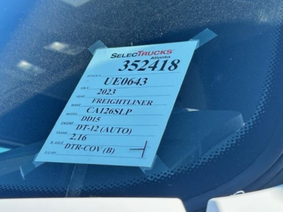 Truck window showing a SelectTrucks tag with stock 352418, VIN 3AKJHHDR7PSUE0643, 2023 Freightliner Cascadia, CA12SLP, engine DT-12 (AUTO), transmission 2.16, DTR-COV (B).