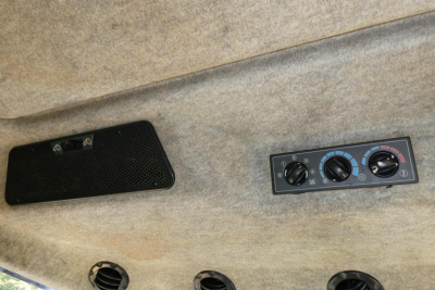 Tractor cabin interior showing climate control panel with three dials and a speaker grill on fabric headliner.