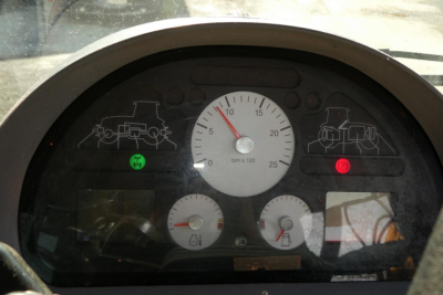 Tractor dashboard panel showing RPM gauge and warning indicators.