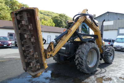 Tractor with front-mounted rear attachment lifting green vegetation muffler