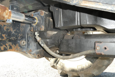 Tractor rear underside showing drive linkage and hydraulic hose routing near suspension and tire.