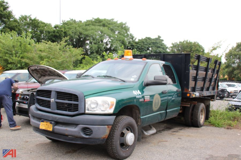 Dodge Ram 3500 dump truck in a parking lot, green cab with orange beacon lights, dump bed behind cab, NY orange license plate, front grill and headlights visible.