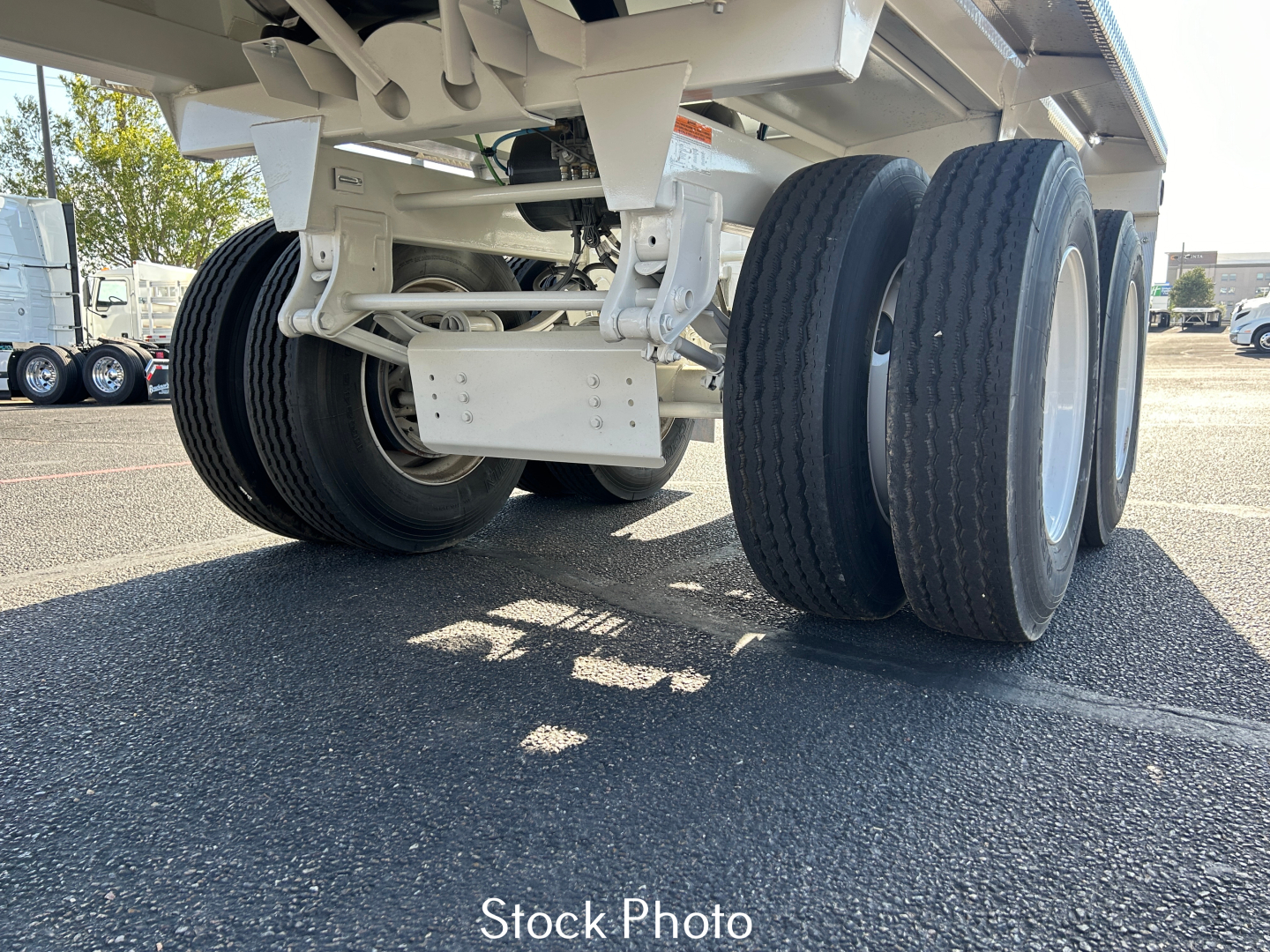 Trailer undercarriage showing dual rear axles and tires with white chassis and suspension components visible.