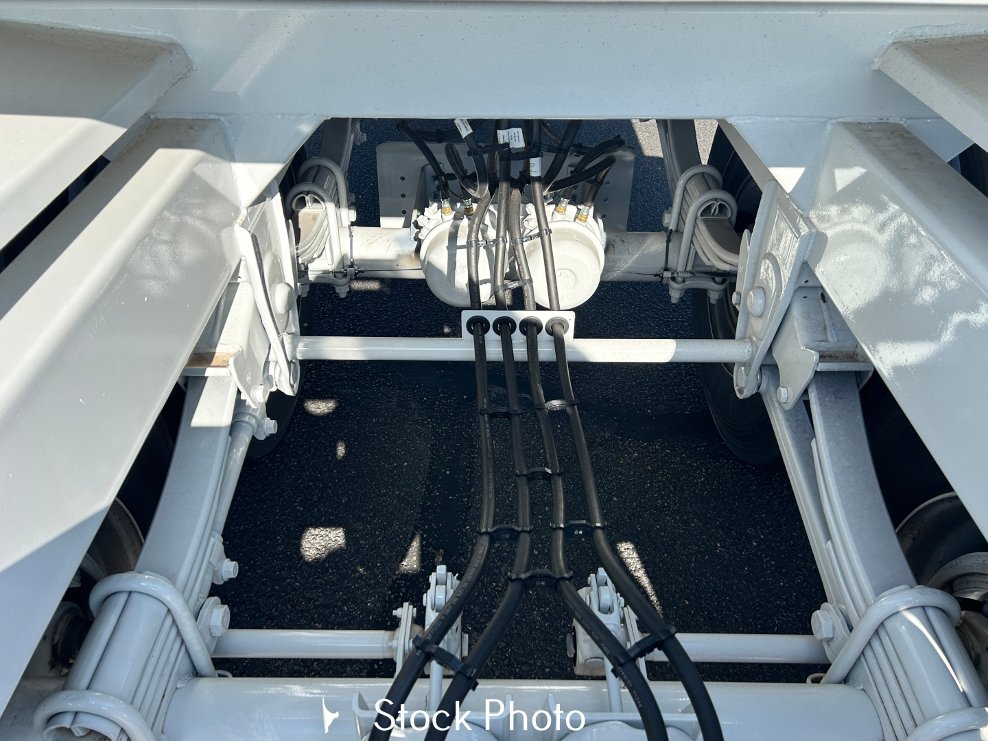 Trailer chassis view showing suspension and power lines; hydraulic or electrical cables visible in center, mounted on a white frame.