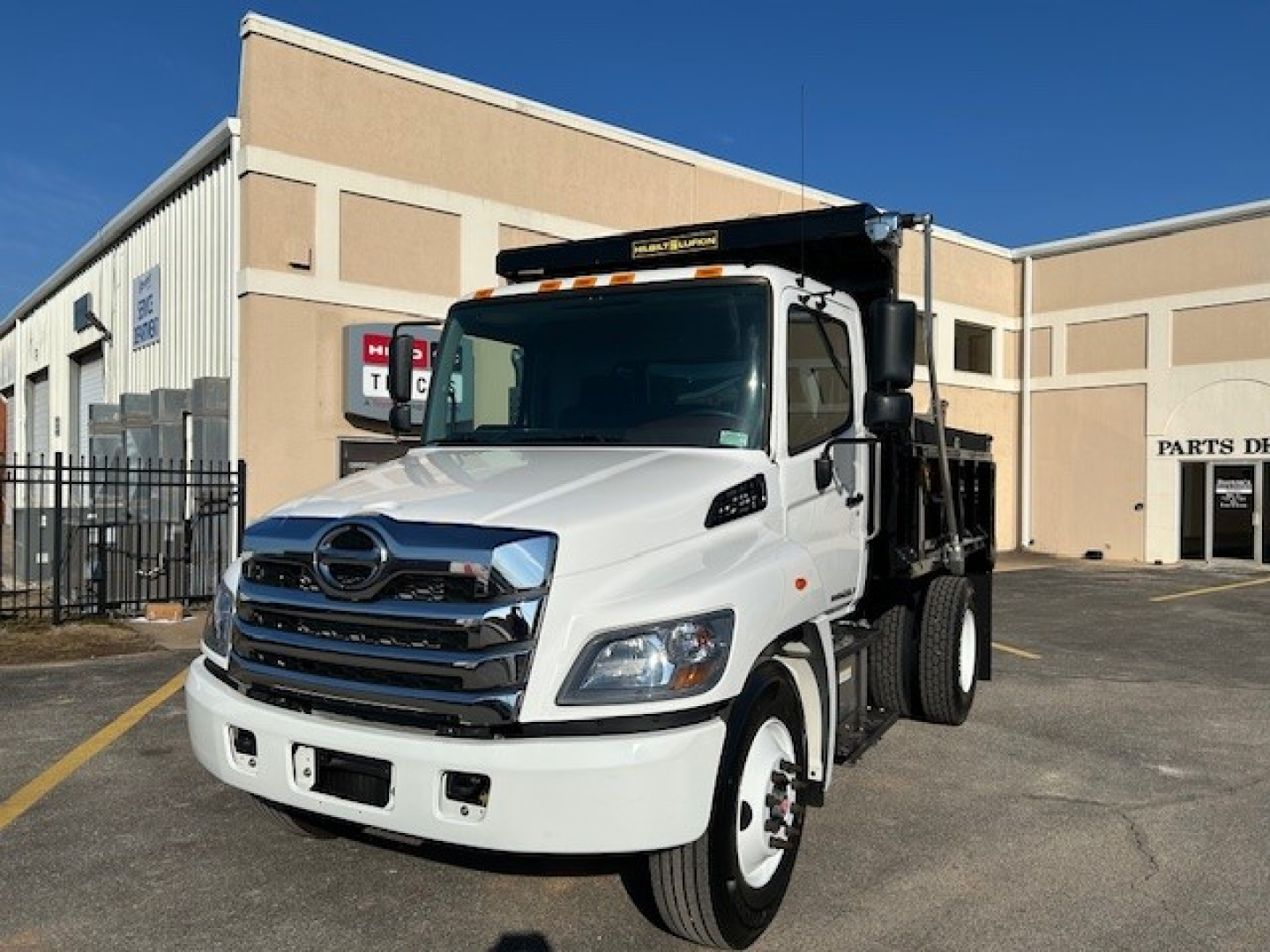 2025 Hino L7 dump truck in white with black dump bed, front grille and chrome bumper. Vehicle shown from front-left angle.