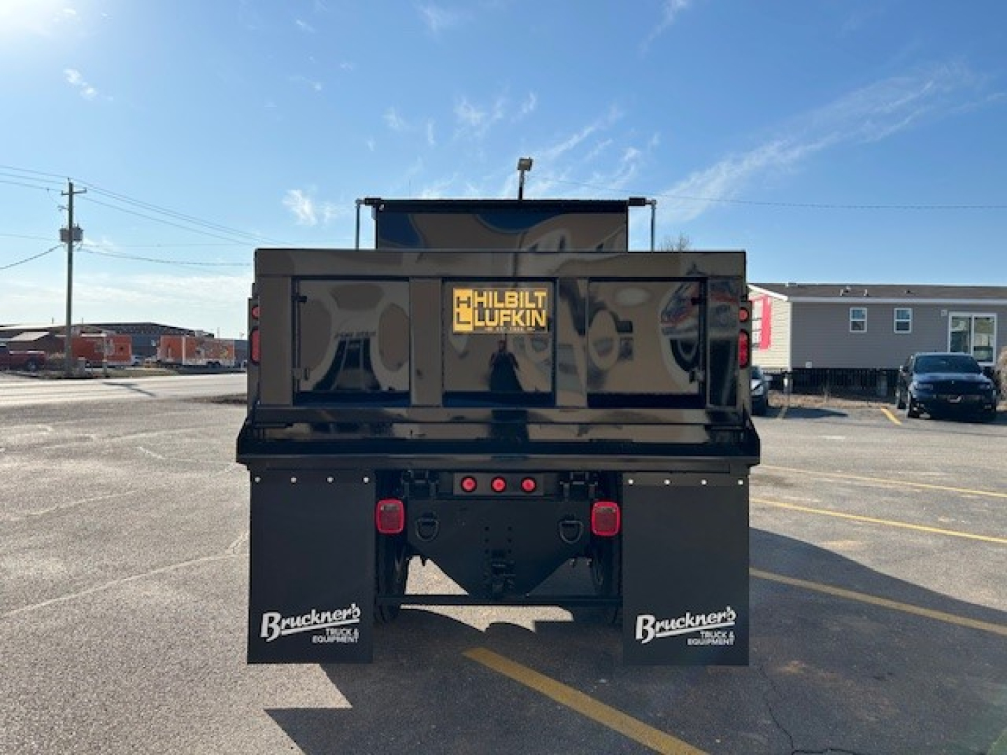 Truck bed rear view of a new 2025 Hino L7 dump truck showing double mud flaps with Bruckner logo and tail lights, stock number 66063, VIN visible.