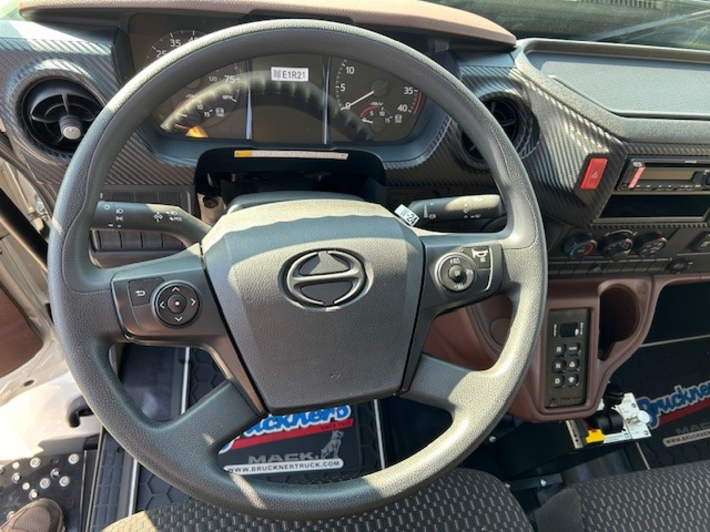 Dashboard and steering wheel of a 2025 Hino L7 dump truck interior showing instrument cluster and steering wheel with Hino logo.