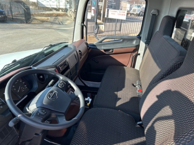 Truck cab interior showing steering wheel with Mercedes logo, dashboard, and bench seat in cabin; brown trim on door panel and gear area visible.
