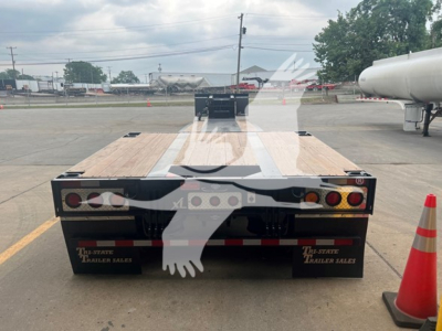 Flatbed trailer rear view showing two tail lights on each side, wooden deck panels, black steel bumper, red and white reflective tape, Dayton-style mud flaps with "TRI-STATE TRAILER SALES" text, and orange traffic cone nearby.